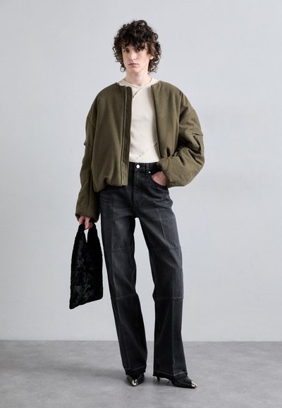 Veste bomber olive, haut texturé crème, jeans noirs taille haute et sac en fausse fourrure noir. Chaussures noires à talons pointus avec accents métalliques.