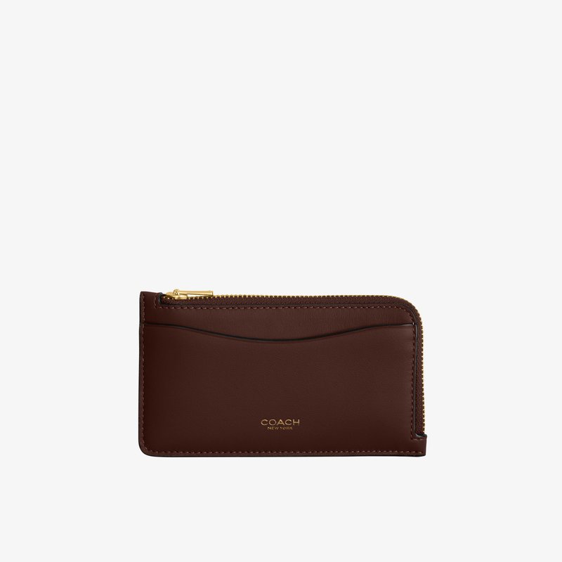 Porte-cartes fin en cuir marron avec fermeture éclair dorée et poche avant, logo Coach New York embossé en or.