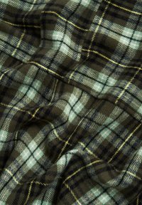 Tissu en flanelle tissé présentant un motif tartan vert et noir, avec des accents bleu clair et jaune, affichant une texture douce et une bonne retombée.