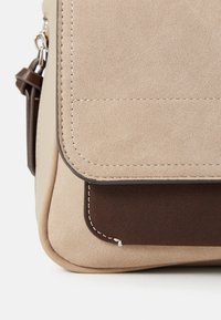 Borsa in pelle scamosciata beige con un accento in pelle scamosciata marrone scuro nella parte inferiore, caratterizzata da cuciture bianche lungo i bordi e un design con chiusura a patta.