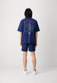 Marinblå kortärmad skjorta med flerfärgad broderad "ADIDAS" och en tropisk design på baksidan; ihop med matchande marinblå shorts.