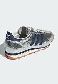 B baskets de sport argentées avec un dessus texturé, rayures navy et une semelle blanche. Dispose d'un design classique à lacets et d'un logo accentué sur le talon.