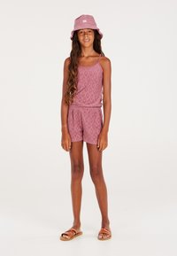 Romper rosa con estampado, tirantes finos y cintura elástica, combinado con un sombrero de cubo a juego y sandalias marrones con tiras cruzadas.