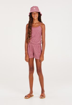 Rompers à motifs roses avec fines bretelles et taille élastique, associé à un chapeau seau assorti et des sandales marron à brides croisées.