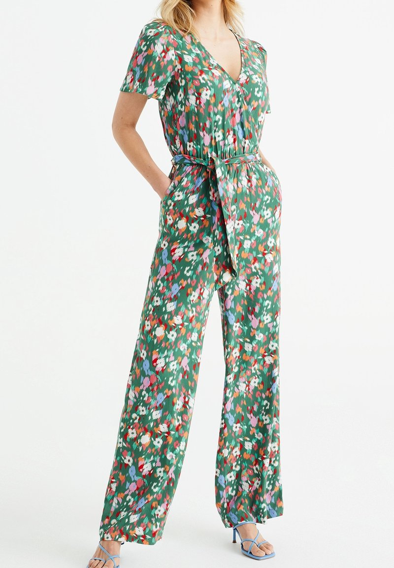 Zelený květinový overal s krátkými rukávy, výstřihem do V, zavázaným pasem, širokými nohavicemi a pestrými vzory. Lehce sepraný materiál s volným vzhledem.