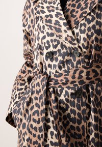 Trench-coat à double boutonnage imprimé léopard avec des boutons noirs et une ceinture en tissu assorti nouée à la taille.