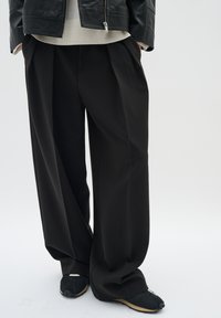 Pantaloni neri a gamba larga con una texture liscia e pieghe frontali, abbinati a scarpe nere con un design testurizzato.