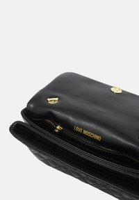 Borsa a tracolla nera in pelle con design trapuntato, hardware dorato e chiusura con zip, con il nome del brand "LOVE MOSCHINO" impresso.