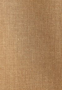 Gros plan sur un tissu en toile de jute tressée marron clair avec une texture rugueuse et des fibres entrelacées en motif quadrillé.