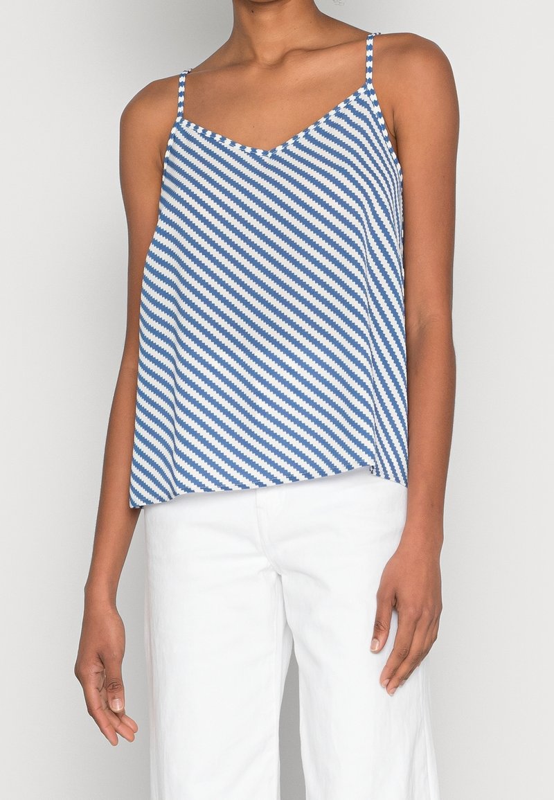 Blå och vit randig camisole med v-ringning, gjord av lätt tyg och tunna axelband, kombinerad med vita byxor.