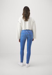 Vit kort tröja med ribbad textur och lätt utsvängda ärmar, kombinerad med blå skinny jeans och avslutad med vita sneakers.