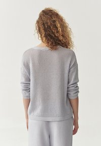 Maglione grigio chiaro a maglia con una vestibilità ampia, caratterizzato da un design a rete, polsini a costine e un ampio scollo. Indossato con pantaloni abbinati grigio chiaro.