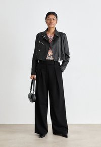Veste en cuir noire courte avec des accents zippés, top à motif zigzag coloré, pantalon noir large taille haute et petit sac à main noir.