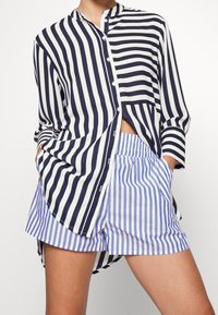 Camicia a righe blu navy e bianca con orlo curvo, abbinata a pantaloni shorts a righe blu e bianche con vita elastica e tasche.