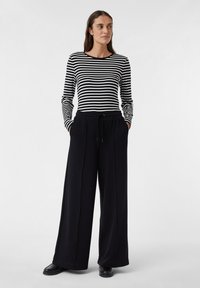Chemise à manches longues avec des rayures horizontales noires et blanches, associée à un pantalon noir ample avec une taille élastique.