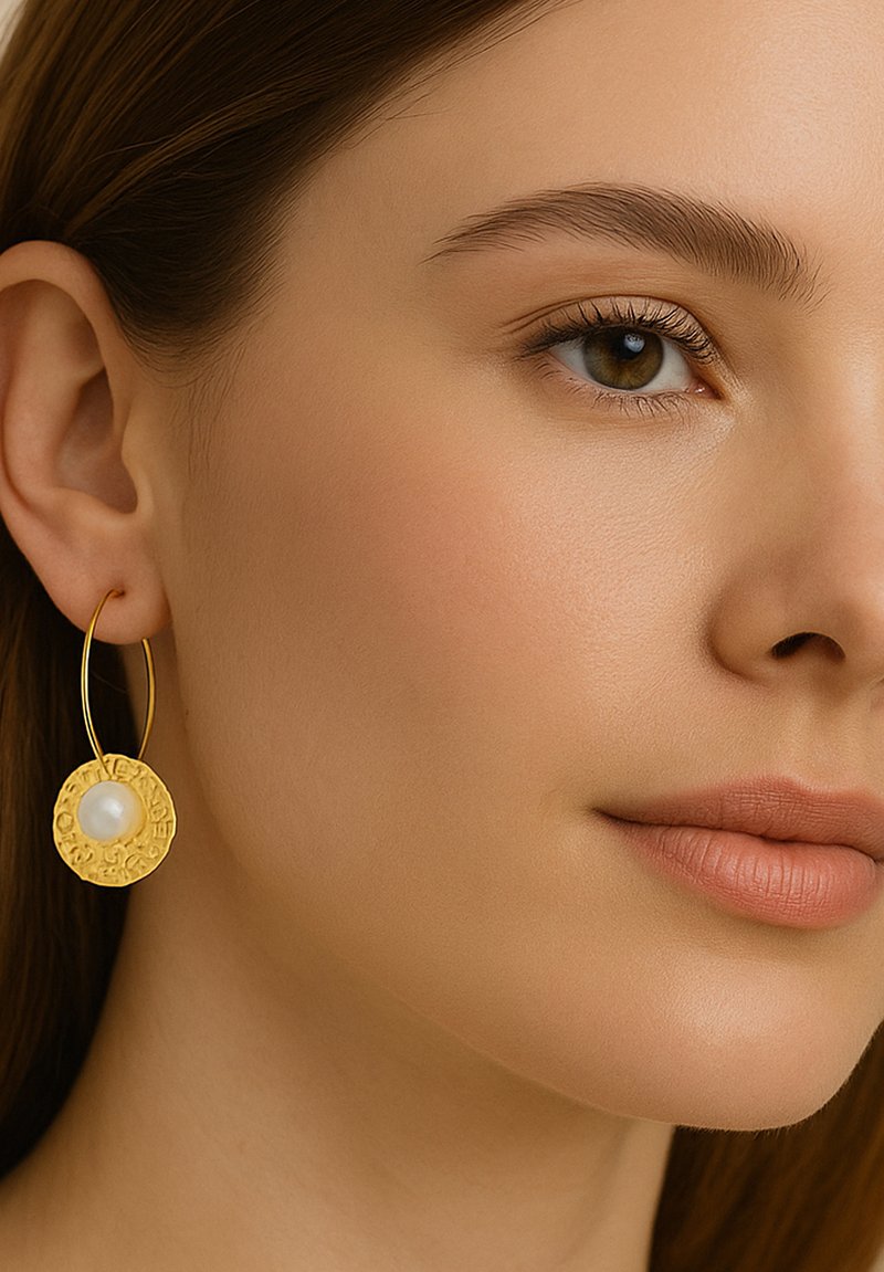 Goldene Creole mit einem strukturierten, kreisförmigen Design und einer zentralen weißen Perle. Glatte Metalloberfläche und kreisförmige Form.