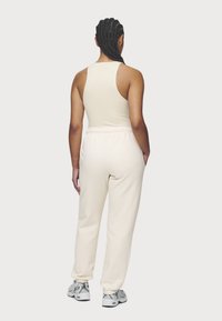 Canotta beige con scollo rotondo abbinata a pantaloni della tuta crema con vita elasticizzata, vista da dietro.