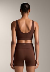 Soutien-gorge de sport marron à côtes avec larges bretelles et short taille haute assorti, présentant un logo discret. Texture lisse, design ajusté.