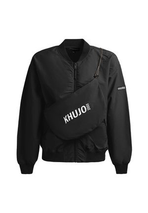 Czarna kurtka typu bomber na zamek z prążkowanymi mankietami i kołnierzem, z czarną torbą na ramię z napisem "KHUJO 2001" w białym kolorze.