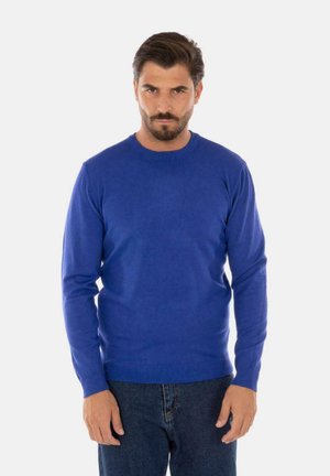 Maglione lungo blu realizzato in morbido tessuto a maglia, con scollatura a girocollo e polsini e orlo a coste, abbinato a jeans scuri.