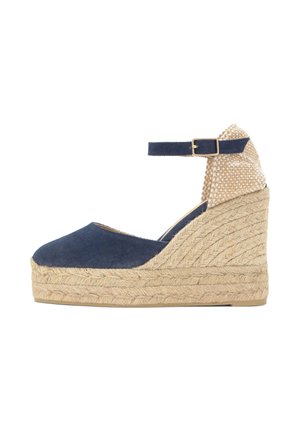 Alpargata cuña azul marino con plataforma de yute trenzado, correa en el tobillo con hebilla dorada y contrafuerte de talón beige texturizado.
