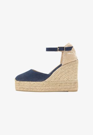 Alpargata cuña azul marino con plataforma de yute trenzado, correa en el tobillo con hebilla dorada y contrafuerte de talón beige texturizado.