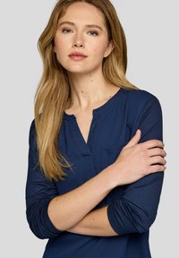 Marineblaue Langarmbluse mit Rundhalsausschnitt, teilweisem Knopfverschluss und einer Brusttasche, aus glattem Stoff mit figurnahem Schnitt.
