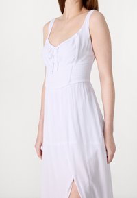 Vit ärmlös klänning med en texturerad överdel, rynkad midja och en hög slits vid låret, med dragsko-detalj vid halsringningen.