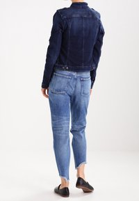 Džínová bunda v tmavě modré barvě s úzkým střihem, zvýrazněná knoflíkovými detaily. Světle modré džíny s rovnými nohavicemi a roztrhaným lemem. Černé baleríny.