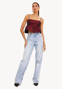 Rode bloemen peplum crop top met dunne banden, gecombineerd met lichtblauwe high-waisted wijde jeans en zwarte puntige hakken.