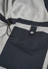Close-up of grey fabric garment with dark blue pocket featuring a snap button and black drawstring with plastic toggle.