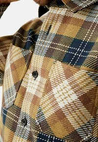 Ruitjespatroon flanellen overhemd in bruin, marineblauw en beige, voorzien van een knoopsluiting, een borstzak en een gestructureerde stof met duidelijke patronen.