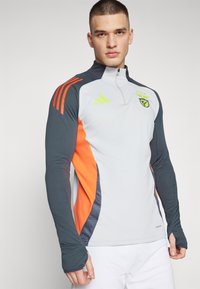 Long-sleeve athletic top in light grey with dark grey and orange accents, featuring a high collar, quarter zip, and layered design elements.