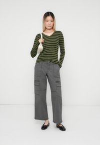 Green and black striped long-sleeve top, gray wide-leg cargo pants with pockets, black flats, and a small white handbag. Plain background.