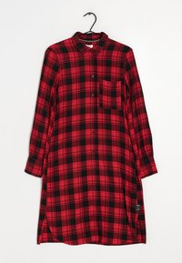 Červené a černé kostičkované košilové šaty s dlouhými rukávy, zapínáním na knoflíky, náprsní kapsou a zakřiveným lemem. Vyrobeno z texturované látky.