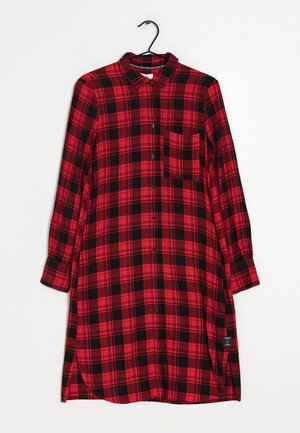 Abito camicia a quadri rosso e nero con maniche lunghe, chiusura con bottoni, tasca sul petto e orlo curvato. Realizzato in un tessuto testurizzato.