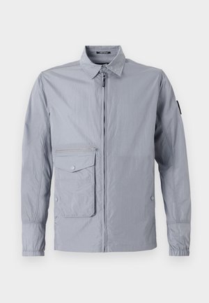 Veste coupe-vent gris clair avec un col, fermeture éclair à l'avant et une poche latérale. Possède des poignets élastiques et une texture lisse et brillante.