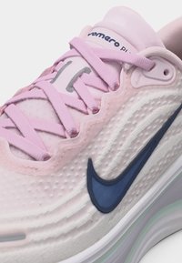 Nærbilde av rosa Nike-løpesko med lys lilla lisser, teksturert side og mørk blå Nike-swoosh-logo.