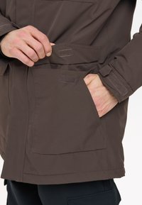 Braune wasserdichte Jacke mit aufgesetzten Taschen und Klettverschlüssen. Sie bietet eine glatte Textur und verstellbare Manschetten für eine sichere Passform.