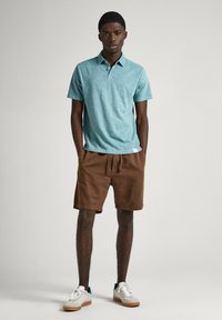 Mörkblå herrpikétröja med texturerad yta, kombinerad med bruna shorts och vita sneakers. Avslappnad design med ledig passform.