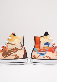 Tenisky s vysokým střihem s barevnými grafikami kreslených postaviček. Materiál je textil s gumovou podrážkou, černým lemem a bílými očky.