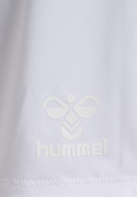 Una tela blanca con una textura suave presenta un sutil logotipo en relieve de un diseño similar a una abeja con el nombre de la marca "hummel" debajo.