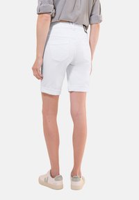 Shorts en denim blanc avec des poignets roulés, dotés de deux poches arrière. Associés à une chemise rayée et des baskets blanches avec des accents verts.