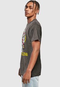 Mørkegrå bomulds t-shirt med rund hals, korte ærmer, og et grafisk design med et farverigt tryk og gul tekst på fronten.