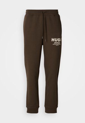 Bruine sweatpants gemaakt van zacht materiaal, met een elastische tailleband met een trekkoord en witte logo-details op de voorkant.