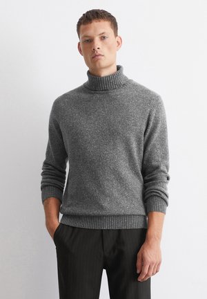 Grau gestrickter Rollkragenpullover mit strukturierter Oberfläche, gerippten Bündchen und Saum. Kombiniert mit schwarzen Nadelstreifenhosen.