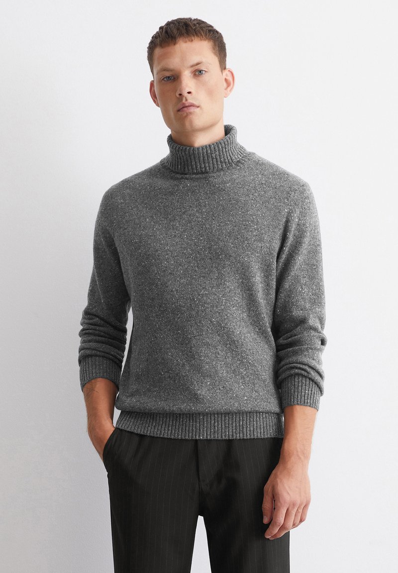 Maglione grigio a collo alto in maglia con finitura testurizzata, polsini e orlo a coste. Abbinato a pantaloni neri a righe sottili.