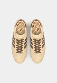 Baskets beiges avec un dessus texturé, des rayures en cuir brun, des lacets bruns et une semelle intérieure à motifs arborant le logo de la marque.