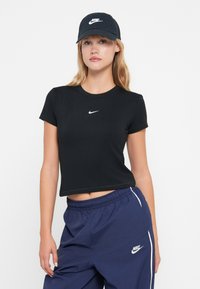 Černé zkrácené tričko s krátkým rukávem a bílým logem Nike. Spárováno s námořnickými modrými kalhotami s bočními pruhy a logem Nike.