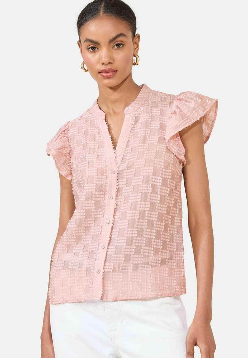 Blusa rosa a maniche corte con motivo testurizzato, dotata di bottoni frontali e maniche arricciate. Realizzata in tessuto leggero e trasparente.